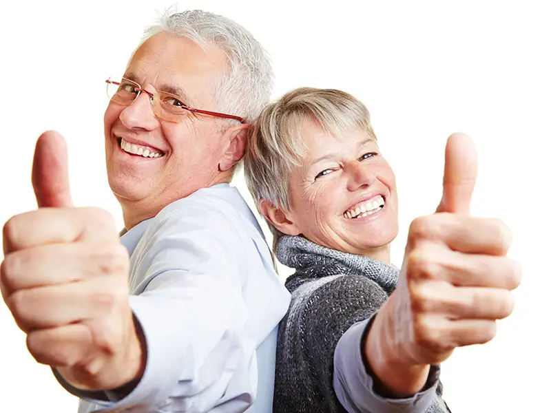 Image of an elderly couple smiling and doing the thumbs up sign.